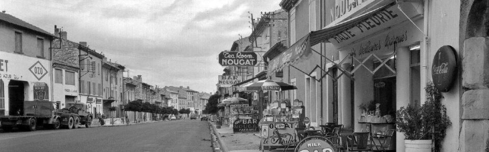 RN7 et rue principale de Montélimar dans les années 60 avec de nombreux commerces, entre garage, salon de thé et nougats