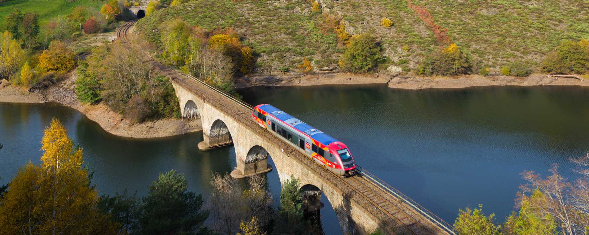 Vue sur un train régional TER SNCF sur un pont au dessus d'une rivière dans un paysage de campagne en montagne